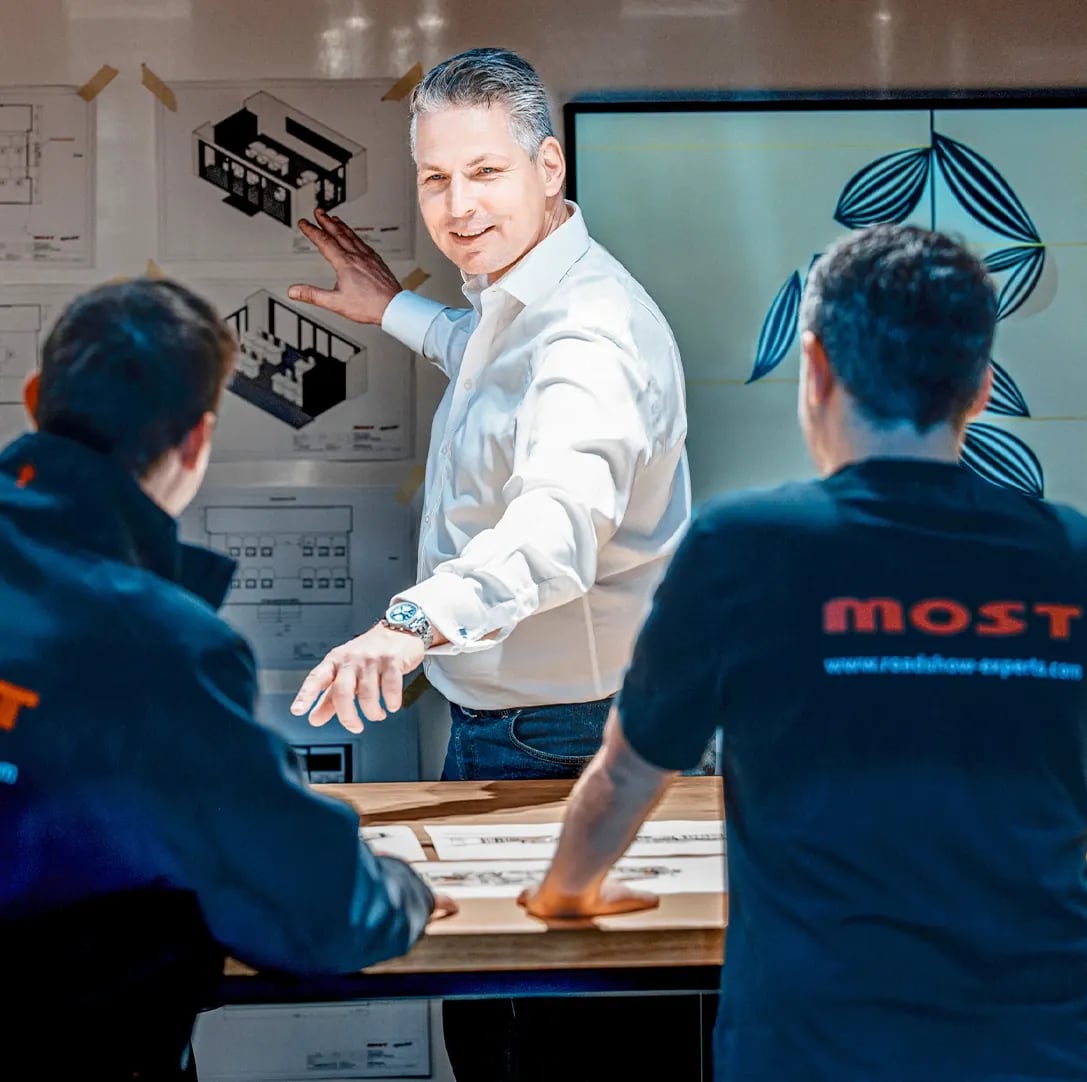 MOST-Projektleiter erklärt an der Wand Grundrisse eines Truck-Innenraums
