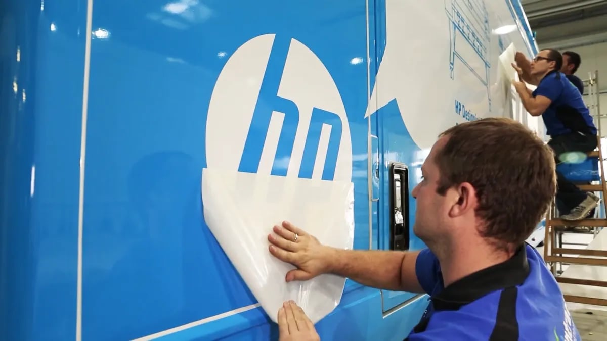 Folierung eines Trucks in der Halle, Mitarbeiter klebt das Logo